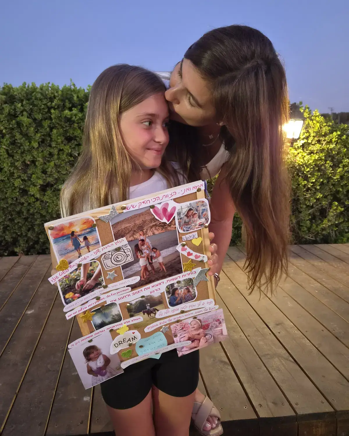 אמא מנשקת את הבת שלה על המצח, והבת מחייכת ומחזיקה את לוח היצירה שהכינו יחד