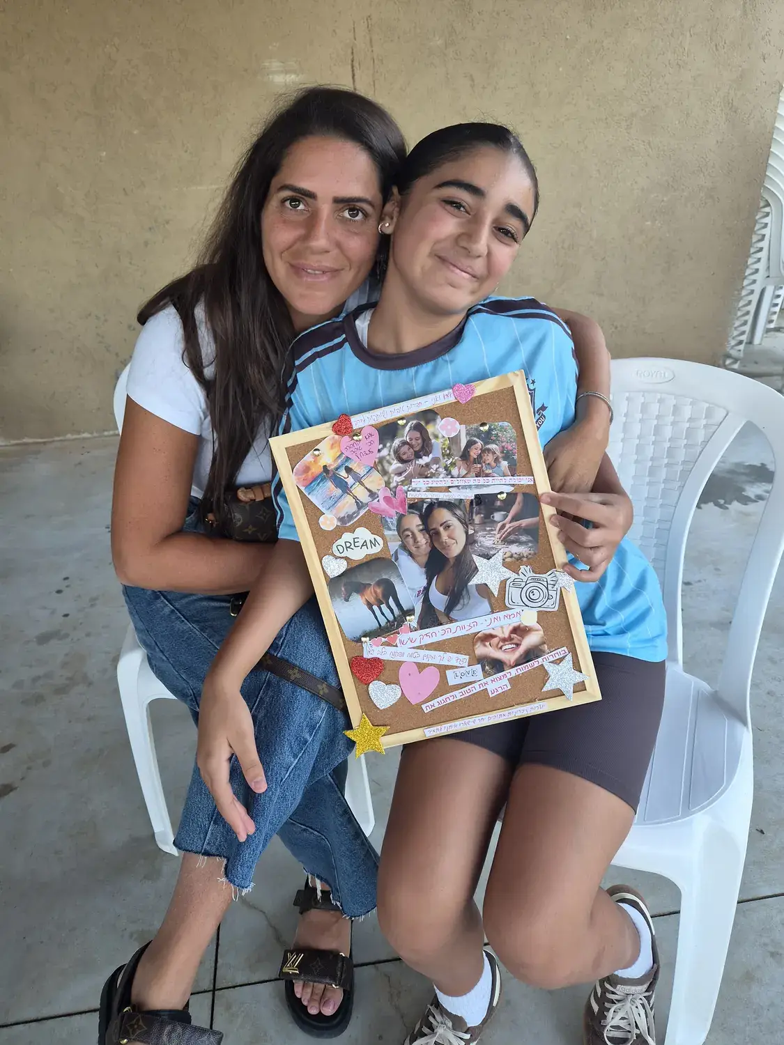 אמא ובת מחובקות, מחזיקות יחד את לוח היצירה שהכינו בסדנה