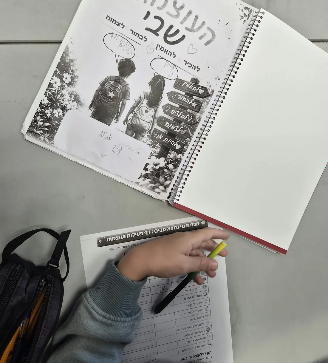 חוברת "העוצמות שבי" פתוחה על שולחן, ויד של ילד כותבת בדף עבודה