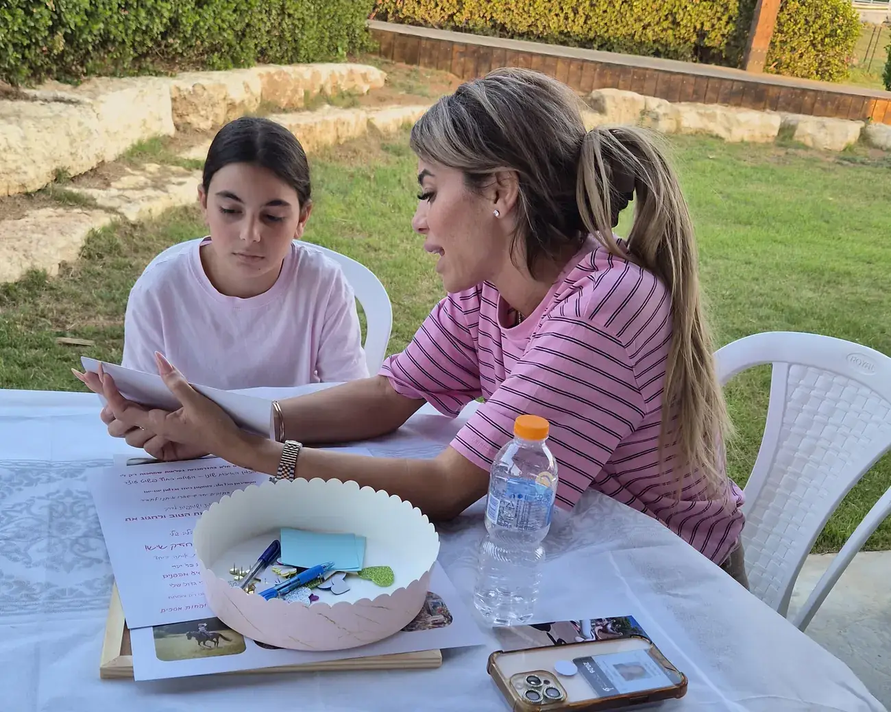 אמא ובת יושבות יחד ליד שולחן היצירה ומסתכלות על דף משותף